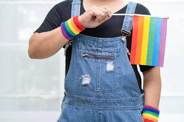 Asian lady wearing blue jean jacket or denim shirt and holding rainbow color flag, symbol of LGBT pride month celebrate annual in June social of gay, lesbian, bisexual, transgender, human rights. - Photo, Image