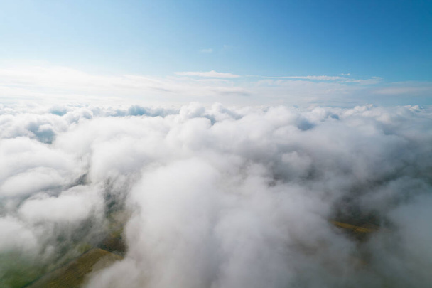 Cumulus clouds, aerial background. Aerial shot with top view of white fluffy clouds gathering. In between the clouds the ground is visible here and there. - Фото, изображение