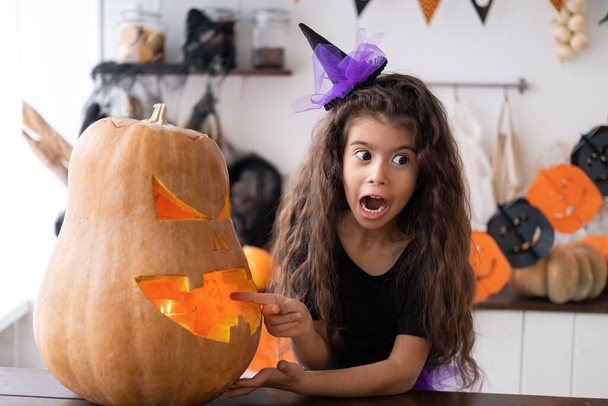 schattig meisje in kostuum van heks met pompoen thuis in de keuken, plezier hebben, vieren Halloween. - Foto, afbeelding