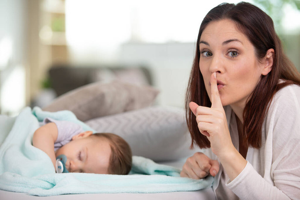woman showing silence sign while cute little baby is sleeping - Fotoğraf, Görsel