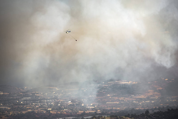 Helicopter with water bucket flying in heavy smoke over rural area, fighting wildfire - Photo, Image
