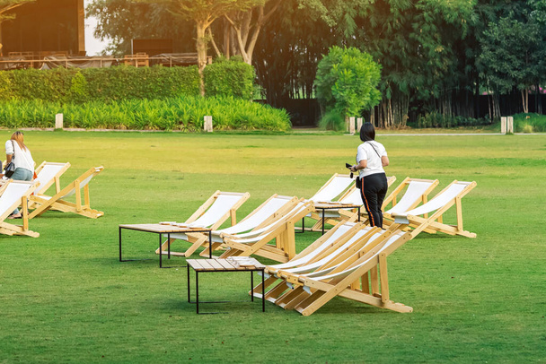 Back view of Asian woman standing among many empty white deck chairs with tables for dinner in lawn is surrounded by shady green grass. Female spending time outside in green nature. Enjoying outdoors. - Photo, Image