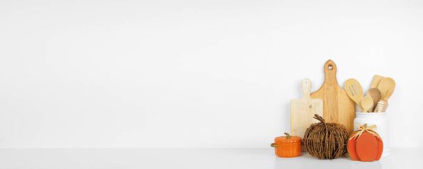 Herbstliches Geschirr, Utensilien und Kürbisdekor auf einem weißen Regal oder einer Theke. Banner vor weißem Hintergrund mit Kopierraum. Herbst zu Hause Küche Kochen Dekor. - Foto, Bild