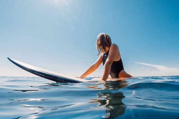 Привлекательная блондинка-серфингистка сидит за доской для серфинга в голубом океане - Фото, изображение