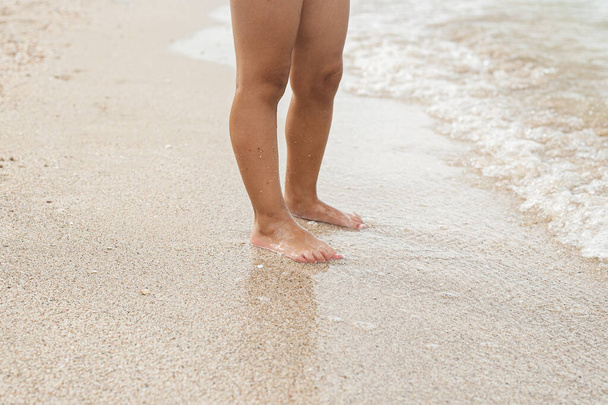 Children's feet stand near the sea on a sandy beach. - Photo, Image