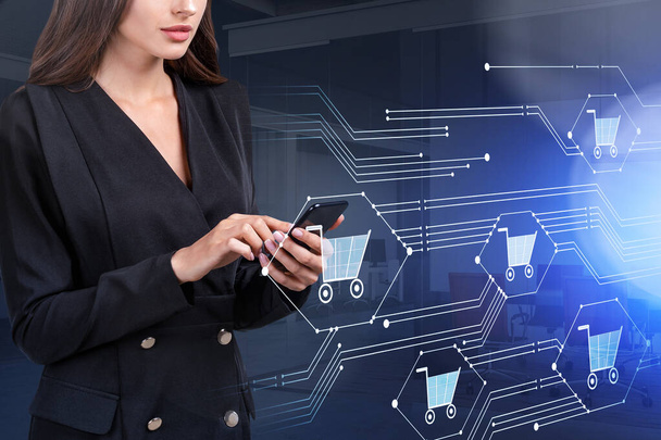 Young attractive businesswoman wearing formal suit is holding smartphone and shopping online. Office workplace in the background. Concept of internet purchasing - Foto, afbeelding
