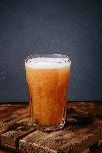 Glass full of golden barrel lager, fresh beer foam, wooden background. Cold drinks, refreshment alcohol beverages. Copy space, vertical shot - Фото, изображение