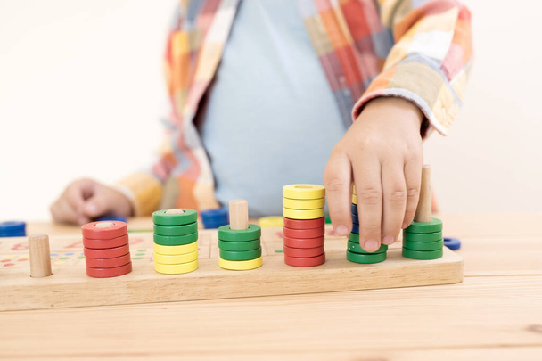 Concept for child math development, learning center, primary school, sorting skills, Montessori. Hands of a Caucasian child playing with a wooden math toy. Number line, counting. Desk.  Close up. - Photo, Image