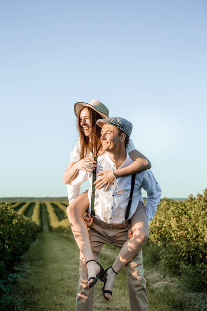 Young beautiful couple in love sitting and hugging in a green field with bushes. Walking in the green field on a sunny summer day. - Foto, Imagem