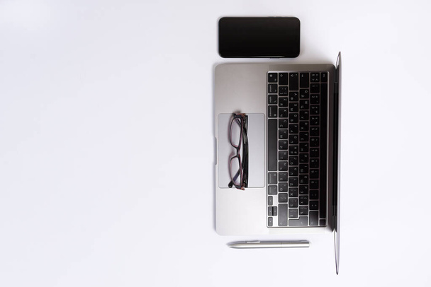 Moderní pracovní prostor s chytrým telefonem, pery, brýlemi a notebookem kopírovat prostor na bílém pozadí. Horní pohled. - Fotografie, Obrázek
