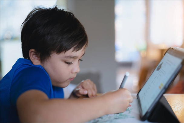 Uczeń za pomocą kolorowego pióra rysunek na białym papierze, Młody dzieciak za pomocą tabletu do pracy domowej w szkole online w Internecie, Happy mieszane dziecko rasy cieszyć malarstwo. Edukacja domowa  - Zdjęcie, obraz