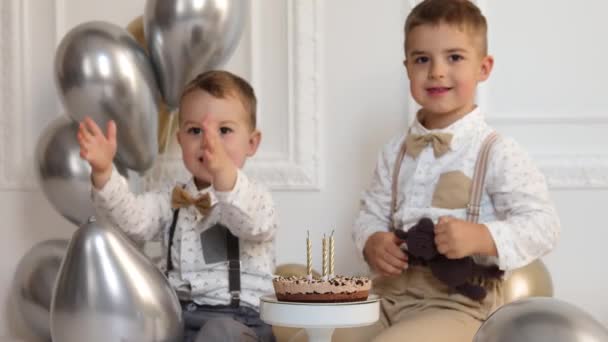 Two boys celebrating birthday, children applauding. Birthday cake with candles and balloons. Happy kids, celebration, white minimalist interior. - Footage, Video