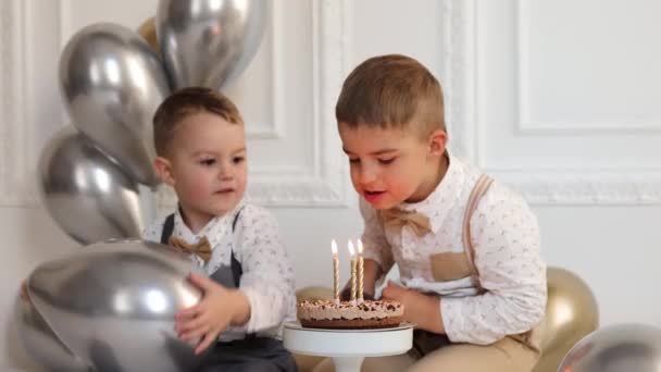 Dwóch chłopców świętuje urodziny, dzieci mają imprezę B-day. Dzieci dmuchają świeczki na torcie urodzinowym. Uroczystość, białe minimalistyczne wnętrze. - Materiał filmowy, wideo