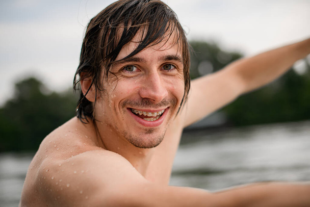 portrait of smiling man with wet brown hair and braces on his teeth - Photo, image