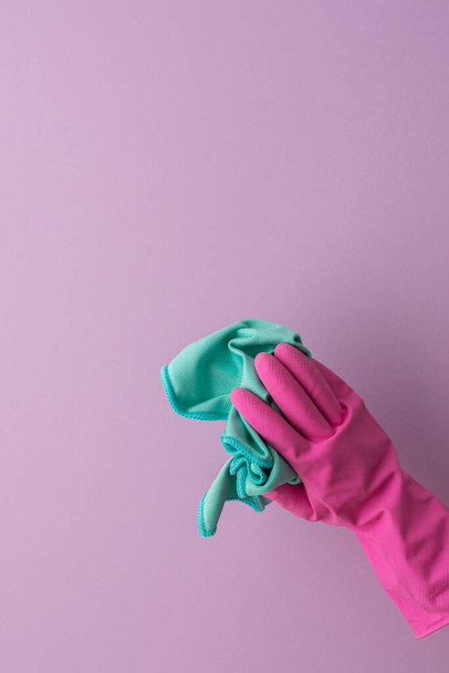 A hand in a pink protective rubber glove holds a microfiber cloth for washing on a purple background - Foto, Bild