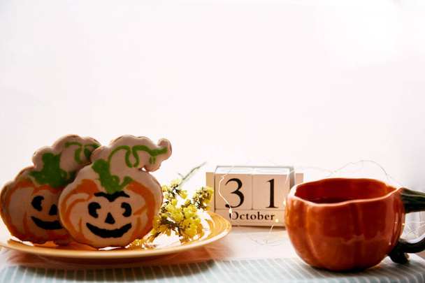 Happy Halloween still life with pumpkin cup and homemade cookies in shape of cute pumpkins and date of Halloween Day. Atmospheric aesthetic autumn holiday concept. Rural life - Photo, Image