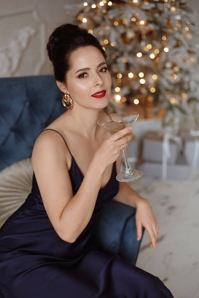 Model woman with a glass of champagne at New Year party, drinking champagne over holiday festive lights background. Beauty woman with perfect fashion makeup - Photo, Image