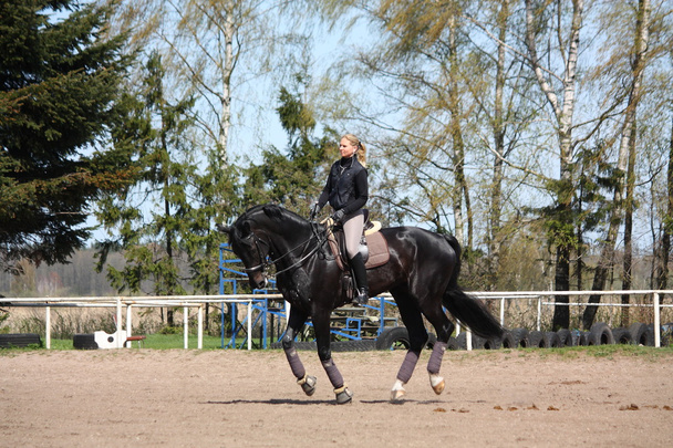 Blonde woman riding black horse - Photo, Image