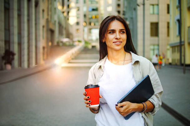 Zdjęcie niezależnej kobiety pijącej kawę podczas pracy na zewnątrz na laptopie podłączonym do publicznego Wi-Fi. Stylowa uczennica studiuje online w mieście. - Zdjęcie, obraz