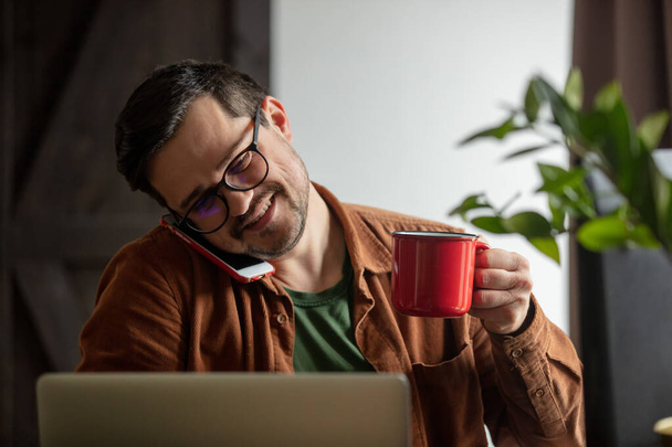 Втомився розробник, що працює з ноутбуком, п'є каву і телефонує по мобільному телефону вдома
 - Фото, зображення