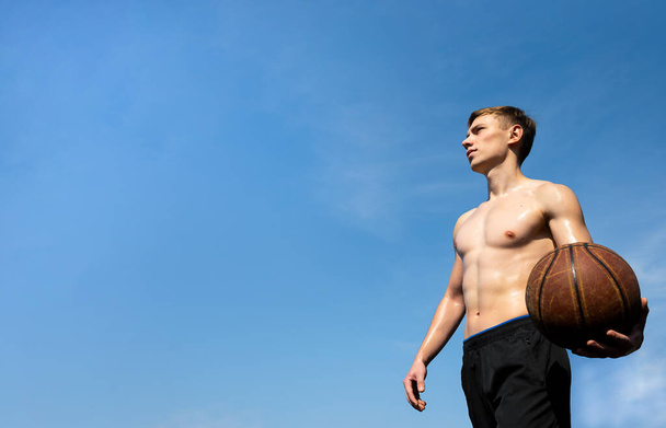 muscular young sportsman with basketball ball outdoors against sky background - Photo, image