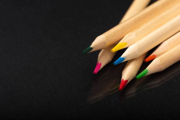 Multi-colored wooden pencils. Dark black background. Natural materials. Stationery. Office tools. Back to school. Education and art. Free space for text. - 写真・画像