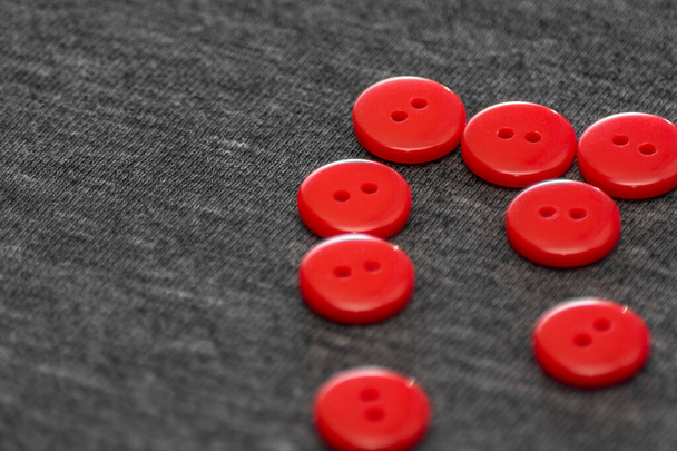 Botones rojos brillantes. Tejido gris. Fondo borroso. El concepto de la industria de la ropa y la decoración. - Foto, imagen