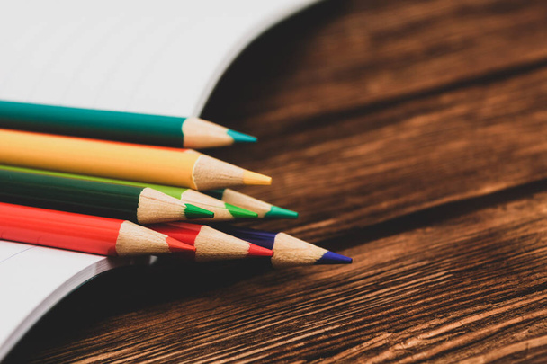 Colored pencils in an open notebook on a dark brown wooden surface. Back to school. Education. Office tool. Empty place for text. - Fotografie, Obrázek