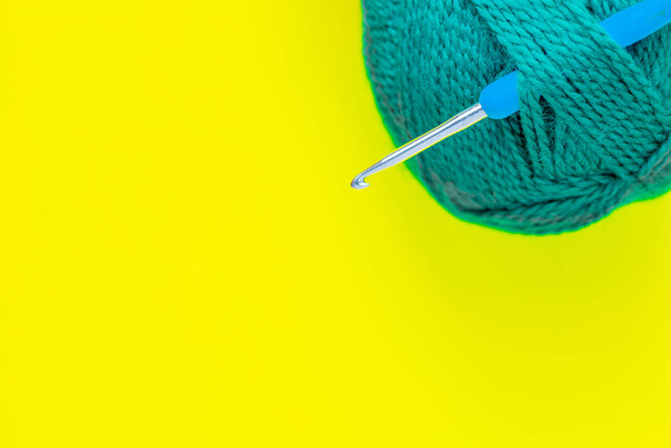 A metal hook with a blue handle is inserted into a skein of green yarn in the upper corner of the photo on a yellow background. top view, flat lay, copy space, isolate. - Photo, image