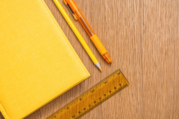 Žlutý zápisník, žluté pero, žlutá tužka a žluté pravítko na dřevěném povrchu stolu. Papírnictví stejné barvy. Kancelářské potřeby. Volné místo pro text. Jasná obchodní koncepce. - Fotografie, Obrázek