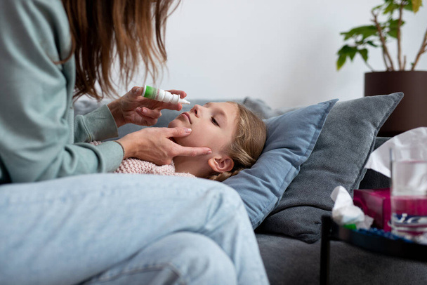 Girl has a runny nose and her mother sprays medicine into her nose - Photo, Image