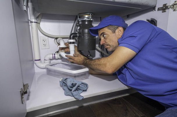 Водопроводчик работает на трубах под кухонной раковиной - Фото, изображение