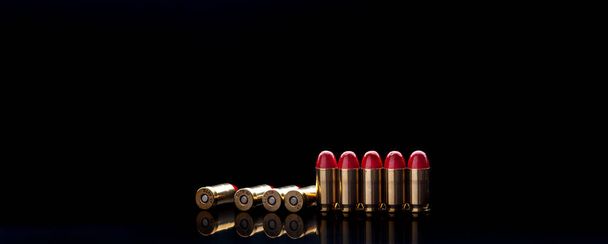 Pistol cartridges with red silicone coating. Bullets for a pistol on a dark background. Reflections on a black surface. - Fotografie, Obrázek