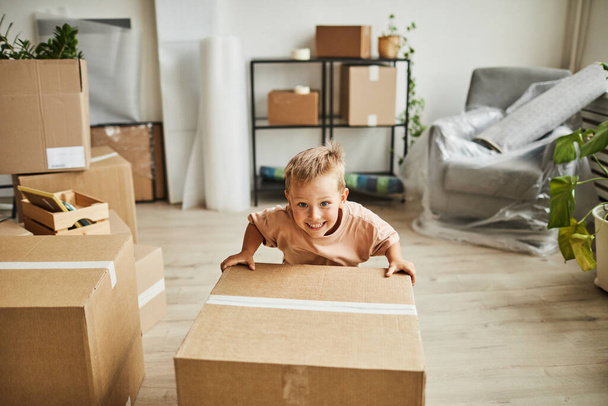 Sonriente niño moviendo cajas en nuevo hogar - Foto, Imagen