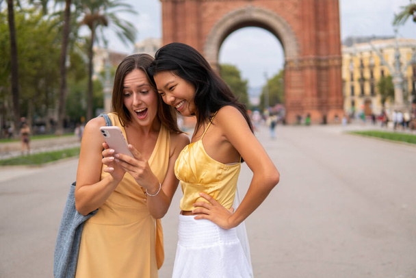 Excited diverse girlfriends using smartphone in city - Photo, Image