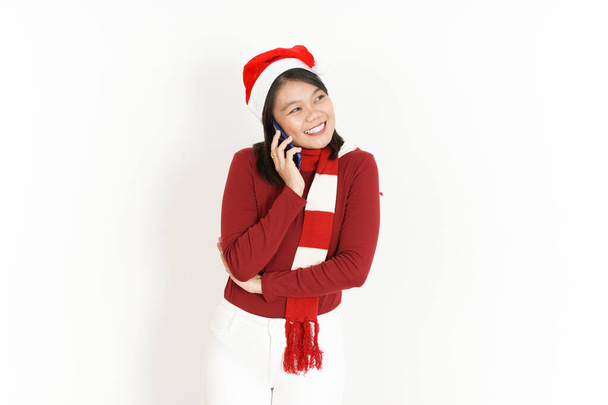 Hablando por teléfono con la expresión de la cara feliz de la hermosa mujer asiática con cuello alto rojo y sombrero de Santa aislado sobre fondo blanco - Foto, imagen