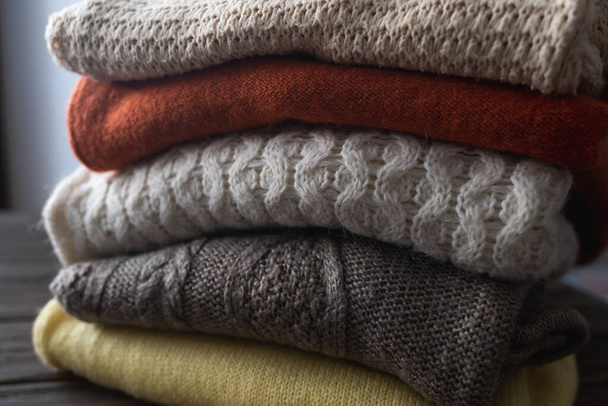 Złożone na drutach ciepłe swetry są ułożone w stosy. Różne wzory na drutach. Jesienne lub zimowe tło. - Zdjęcie, obraz