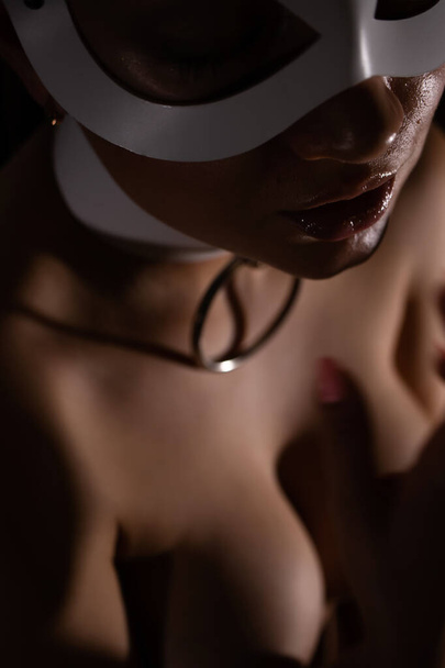 Z góry anonimowa kobieta w masce i kołnierzyku dotykając piersi w biustonosz podczas sesji BDSM w ciemnym pokoju - Zdjęcie, obraz