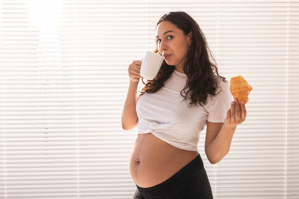 Těhotná žena jí croissant a pije kávu. Těhotenství a mateřskou dovolenou. Kopírovat prostor - Fotografie, Obrázek