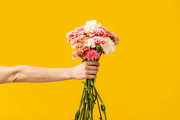 Hand with bouquet of beautiful carnations on color background - Fotoğraf, Görsel