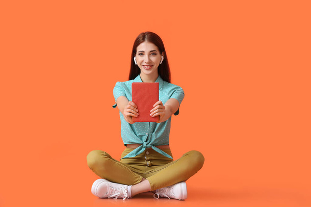 Fiatal nő fülhallgatóval és könyv a színes háttér - Fotó, kép