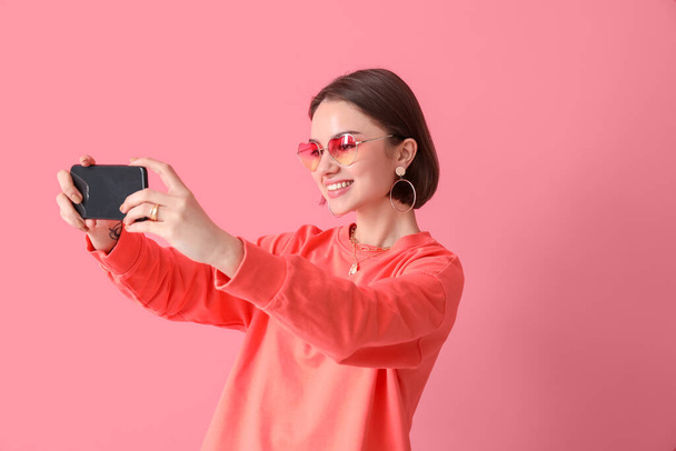 Piękna młoda kobieta robi selfie na różowym tle - Zdjęcie, obraz