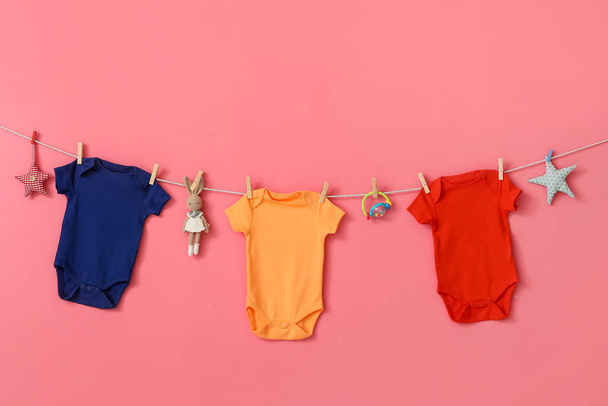 Different baby clothes and toys hanging on rope against pink background - Photo, Image