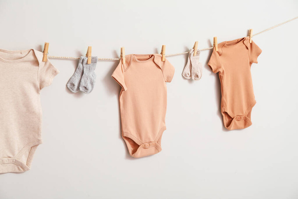 Different baby clothes and socks hanging on rope against white background - Photo, Image