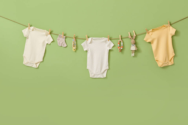 Διαφορετικά βρεφικά ρούχα και παιχνίδια κρέμονται σε σχοινί με φόντο το χρώμα - Φωτογραφία, εικόνα