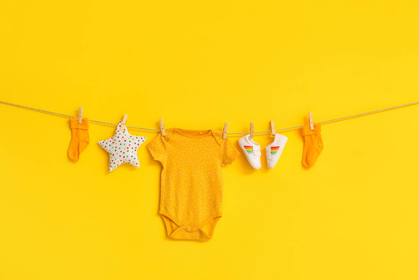 Elegante ropa de bebé, zapatos y juguetes colgando de la cuerda contra el fondo de color - Foto, imagen