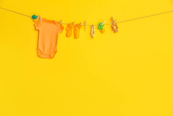 Baby bodysuit, toys and socks hanging on rope against color background - Photo, Image