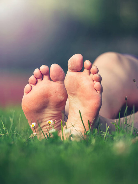 Semelles sales avec peau dure et sèche des pieds nus femme sportive d'âge moyen. Jambes femelles reposant dans l'herbe fraîche du printemps - Photo, image
