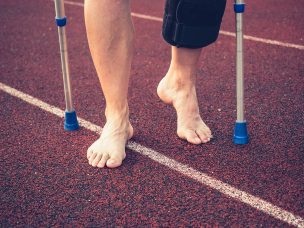 Sattuu urheilu nainen kävelee polvi tuki jälkeen vamman lääketieteen tikkuja. Väsynyt paljain jaloin kypsä nainen. - Valokuva, kuva