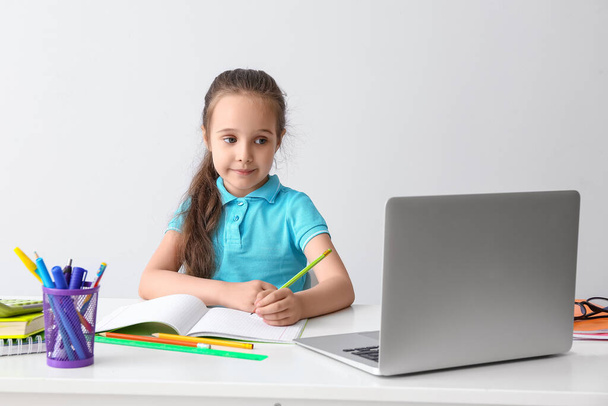 Petite fille faisant ses devoirs à table sur fond clair - Photo, image